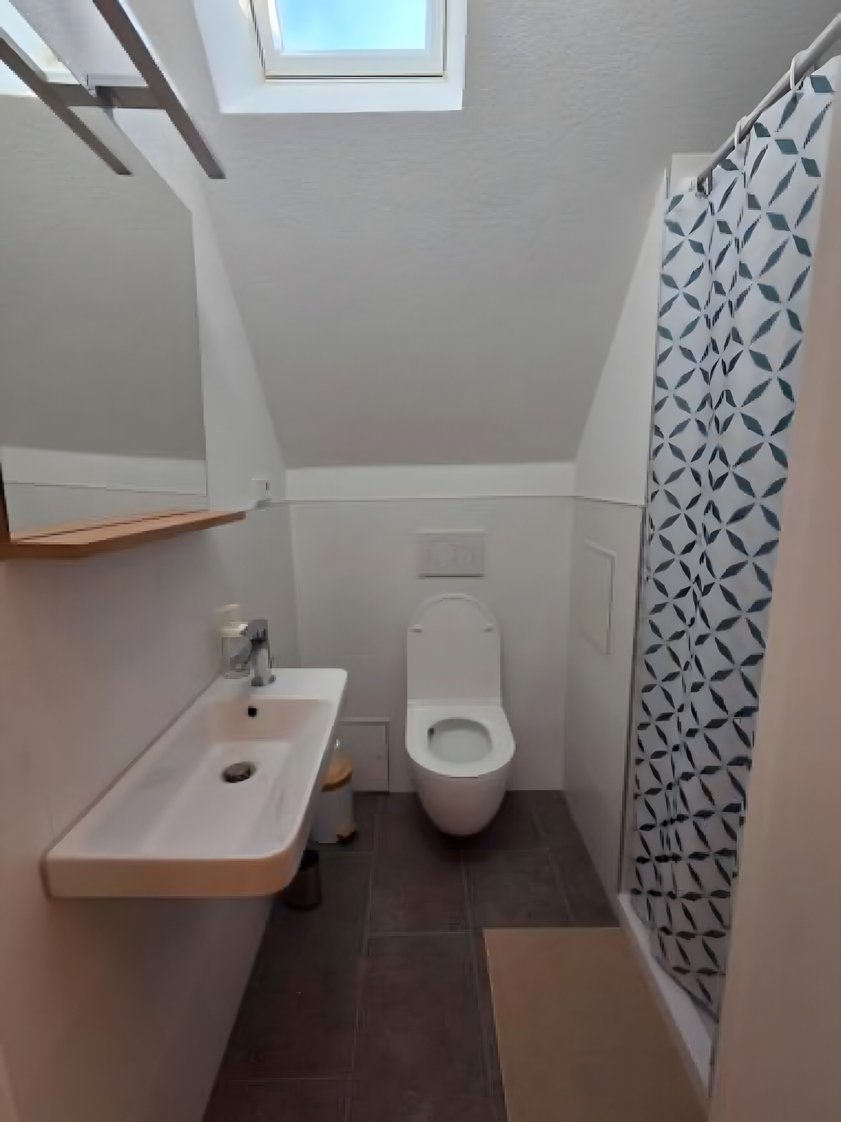 Et lille badeværelse med hvid vask, toilet og brusebad med geometrisk mønster.