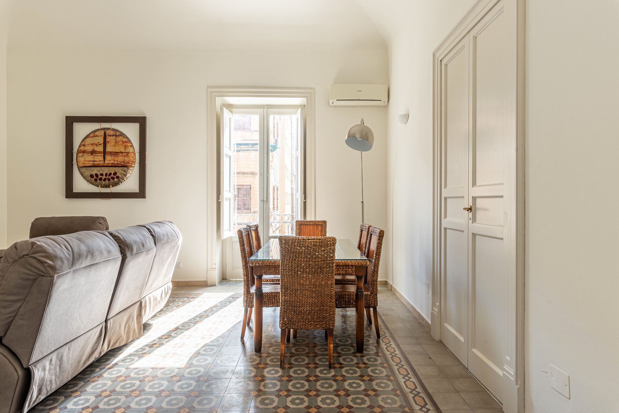 Un espace repas comprenant une table et des chaises, un canapé, un sol à motifs et une porte donnant sur l’extérieur.