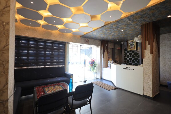 A hotel reception area with a modern design, including a hexagonal ceiling pattern, marble walls, and a reception desk labeled "HOTEL BLUE MOUNTAIN". - Hotel Blue Mountain (Udaipur)