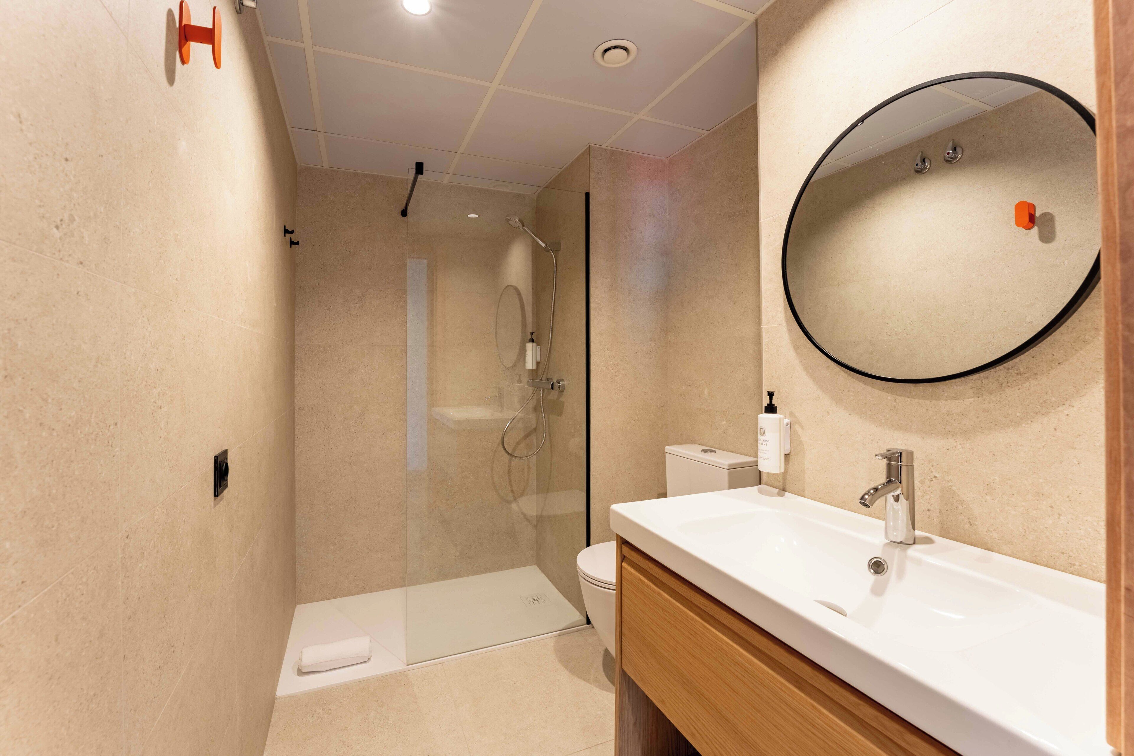 A modern bathroom with a glass-enclosed shower, a white sink, and a round mirror.