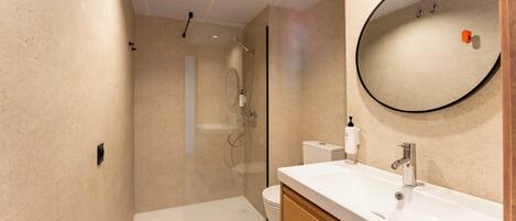 A modern bathroom with a glass-enclosed shower, a white sink, and a round mirror.