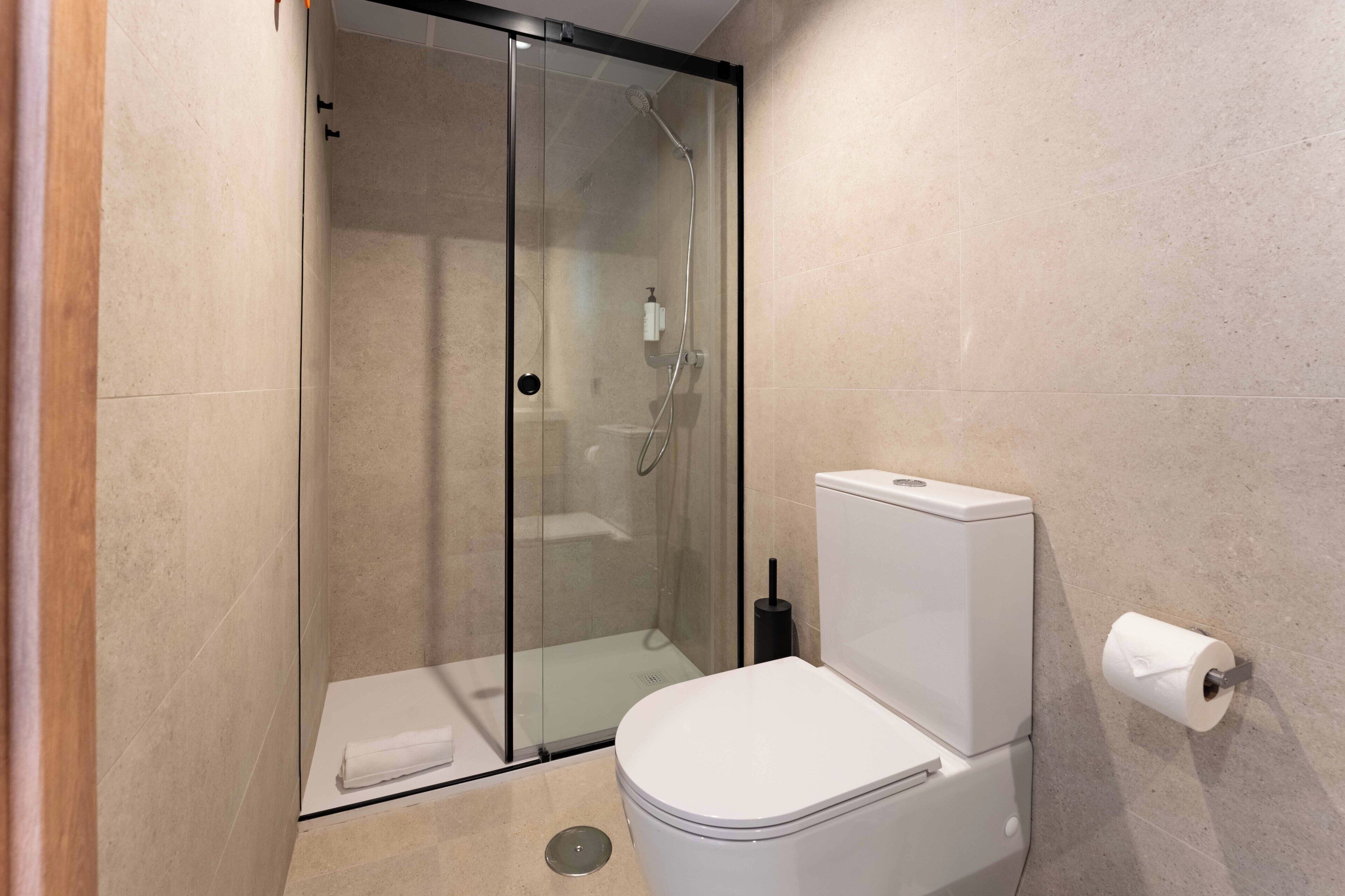 Ein modernes Badezimmer mit einer gläsernen Duschkabine, einer weißen Toilette und einem Toilettenpapierhalter an der Wand.