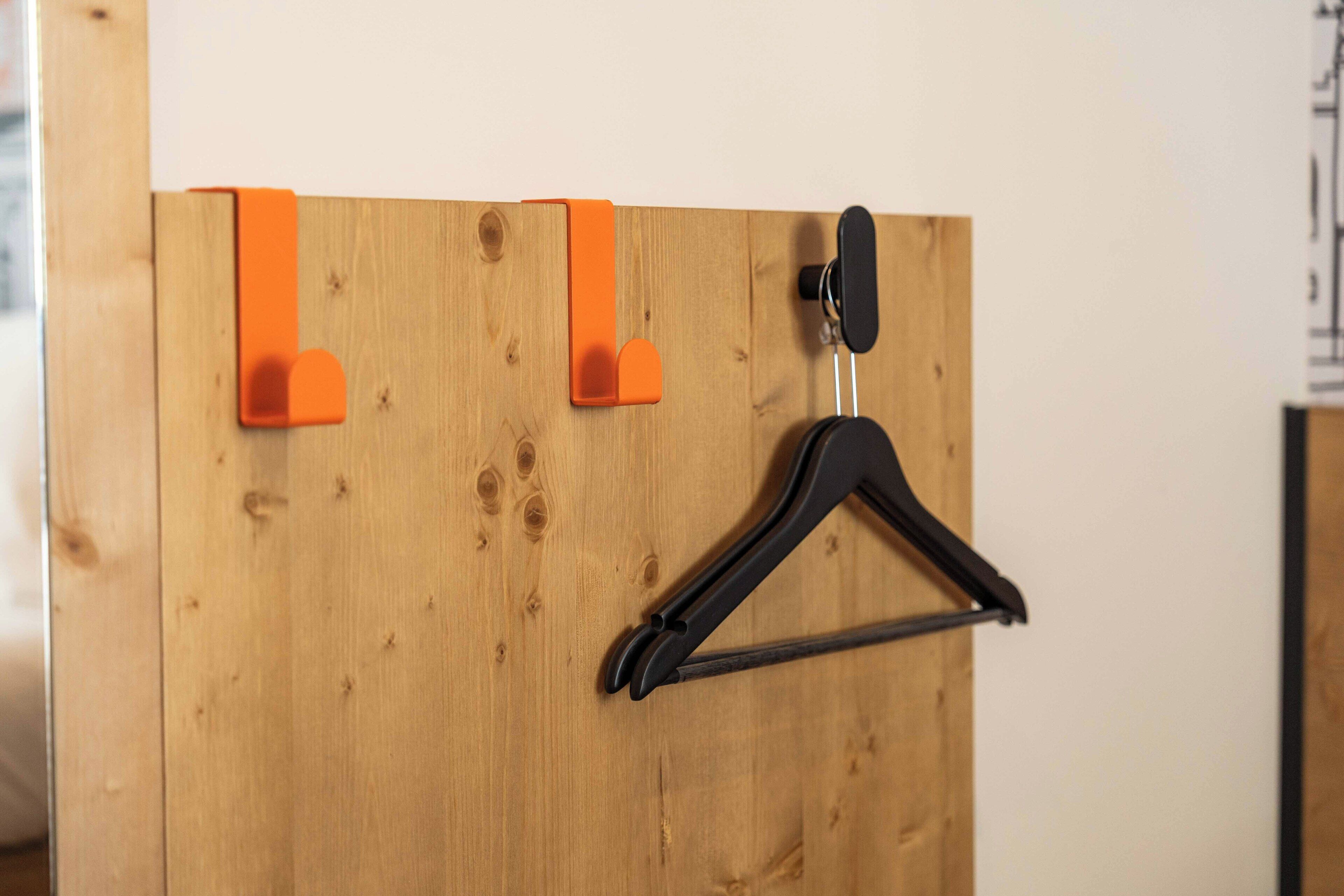 A wooden wall with two orange clips and a black hanger.