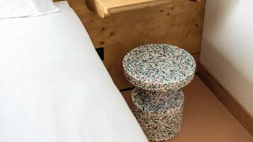 Ein kleiner, runder Hocker mit Blumenmuster, eine Holzbank und ein weißes Bett in einem Zimmer mit Holzwänden.