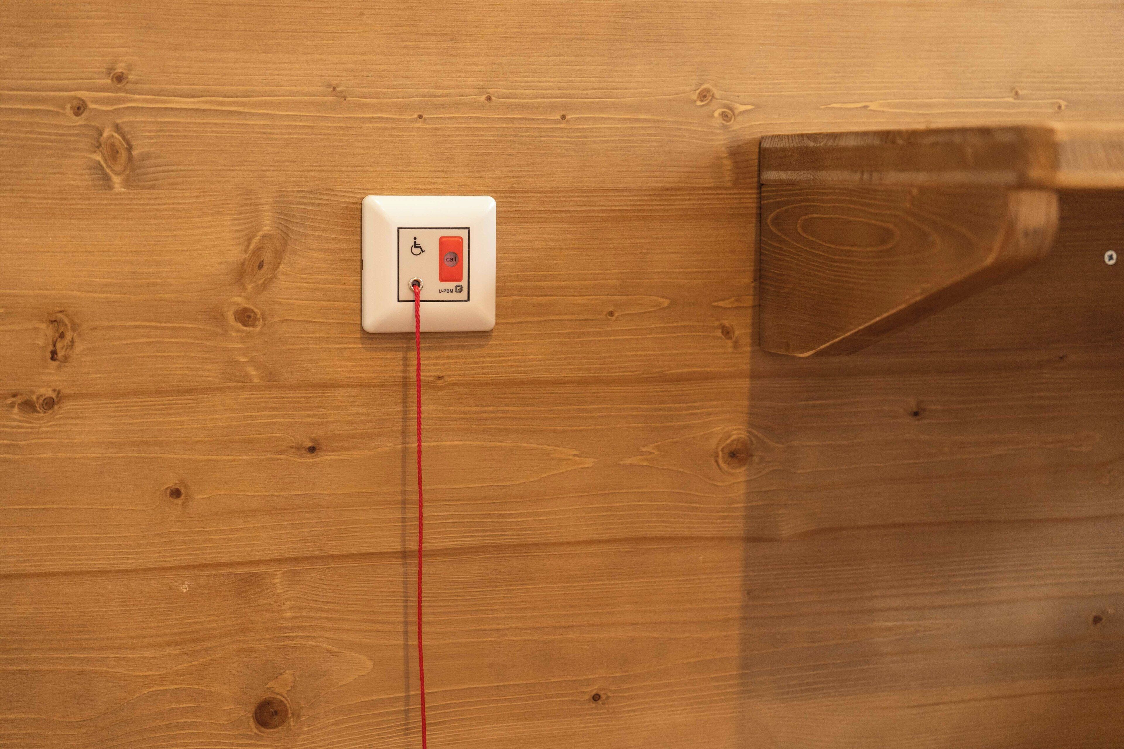 A wooden wall with a white electrical outlet and a red wire.