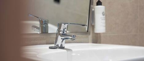 A bathroom sink with a chrome faucet, a mirror, and a bottle of hand soap on the wall.