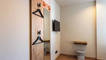 Un pasillo con una puerta de madera, un espejo, un televisor negro montado en la pared, un rascadorito para gato y un estante de madera.