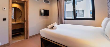 A hotel room with a bed, a television, a window with curtains, a door leading to a closet, and a wall-mounted air vent.