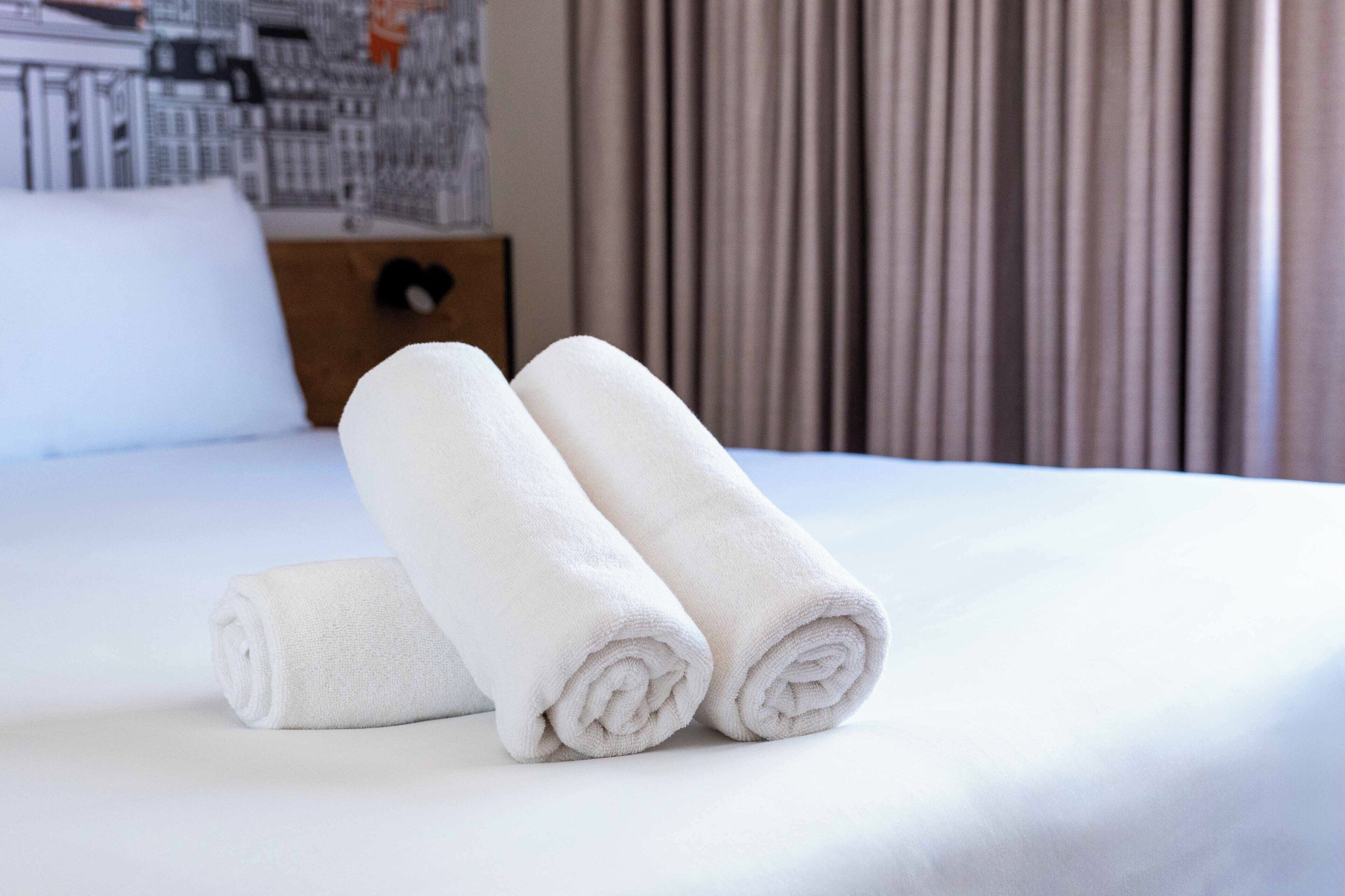 A neatly made bed with two rolled white towels on it.