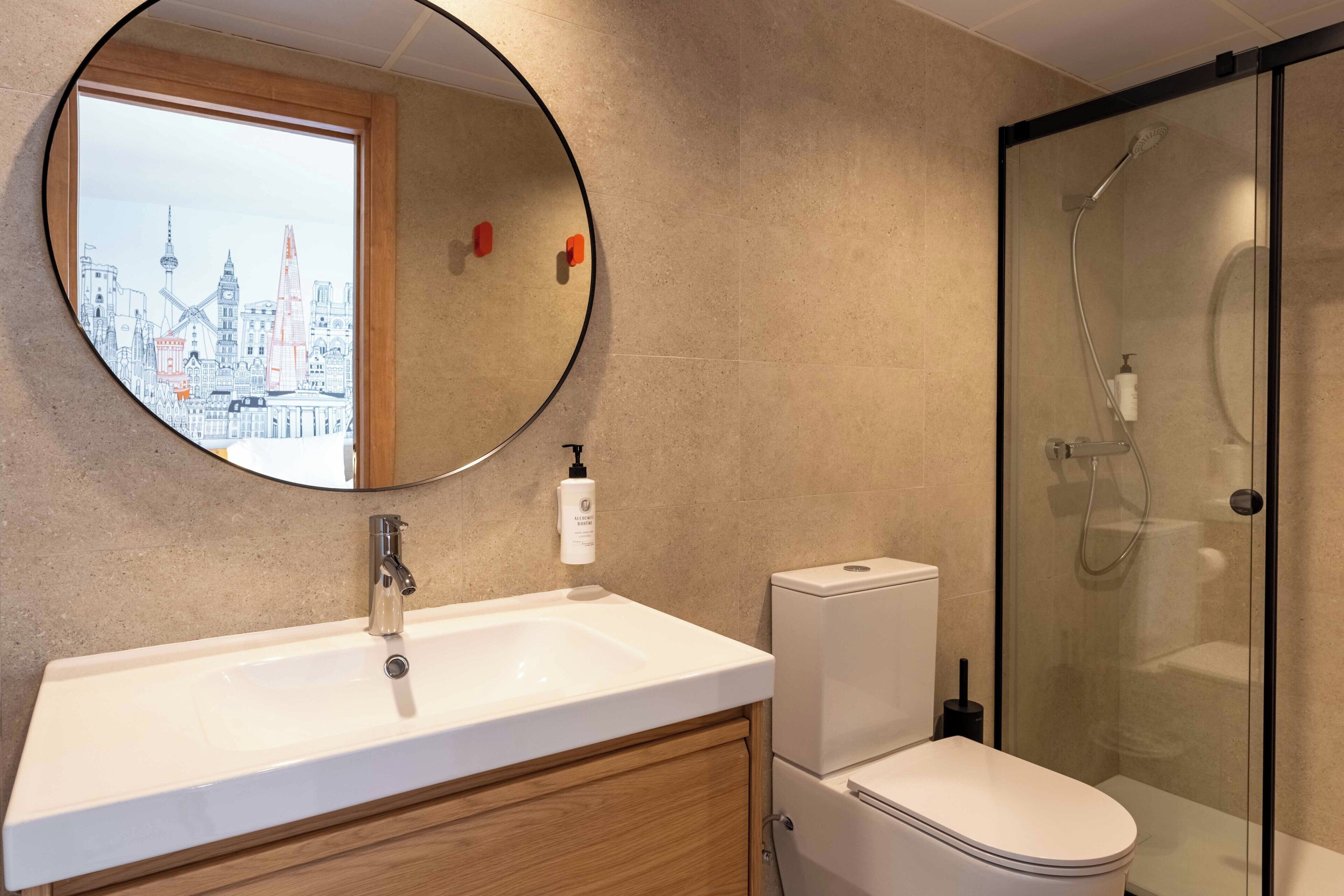 A bathroom with a round mirror, a sink, a toilet, and a glass-enclosed shower.