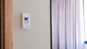 Ein an der Wand befestigtes Thermostat, ein Fenster mit Vorhängen und ein Holztürrahmen.