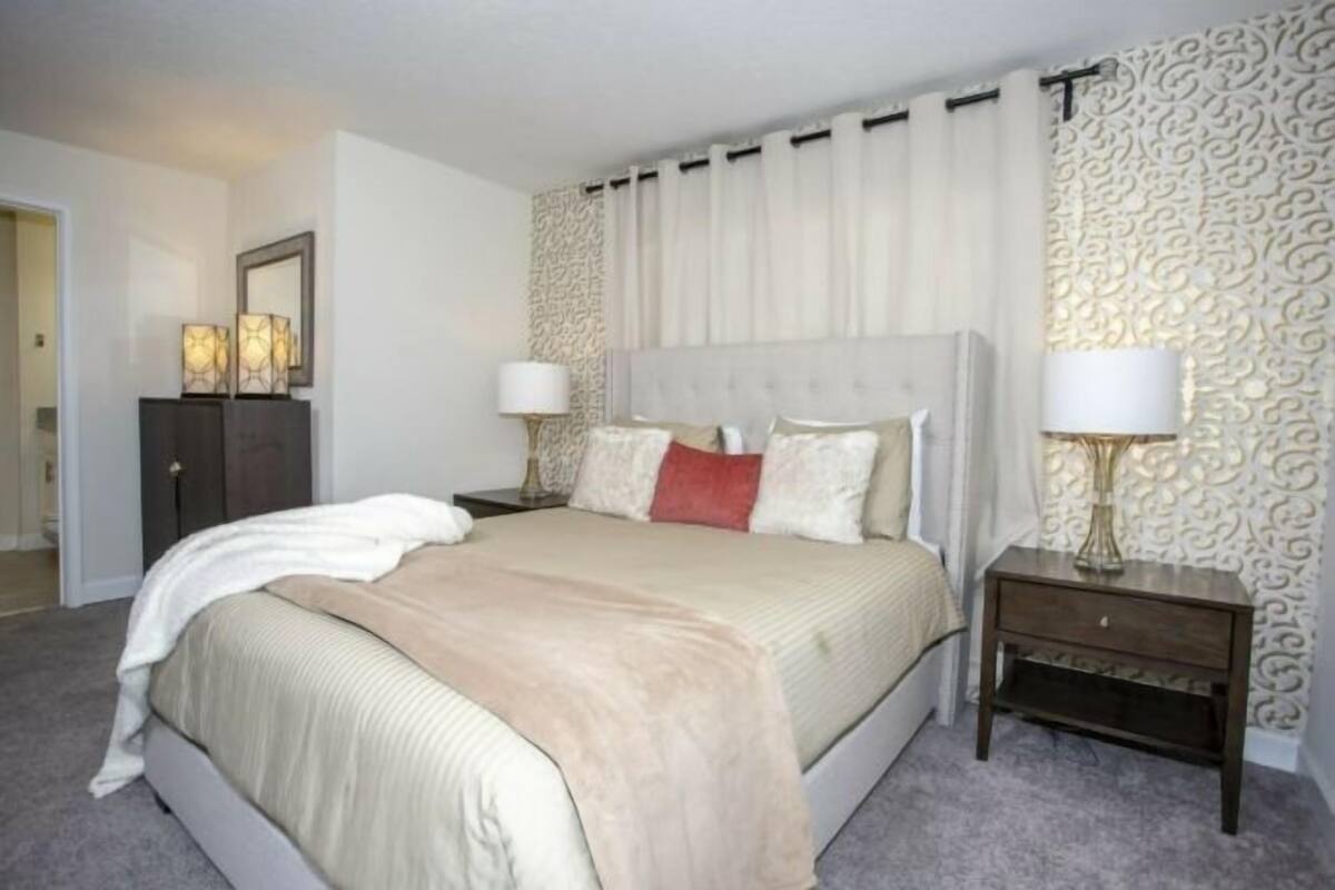 Une chambre à coucher avec un grand lit, deux tables de chevet avec des lampes, un mur décoratif et une porte donnant sur une autre pièce.