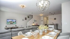 Un comedor moderno con una mesa de madera dispuesta para cuatro personas, un sofá gris y una escalera que sube a otro nivel.
