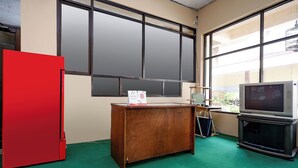 A room with a wooden desk, a red refrigerator, a television, and large windows. - OYO 1706 Hotel H&w Solo (Jaten)