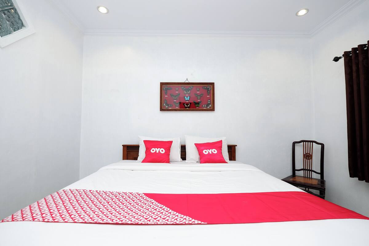A neatly made bed with a red and white patterned bedspread, two pillows with the word "OYO" on them, and a framed picture on the wall above the bed.