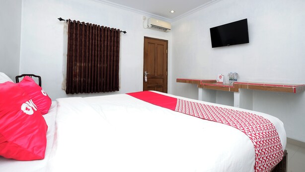 A hotel room with a bed, a TV mounted on the wall, a wooden door, and a window with curtains. - OYO 1706 Hotel H&w Solo (Jaten)