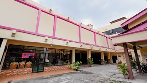 A hotel with a pink and beige facade, large windows, and a covered entrance area with potted plants. - OYO 1706 Hotel H&w Solo (Jaten)