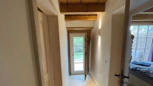 A narrow hallway with wooden beams on the ceiling, a door at the end, and a bed with a mattress and blanket in the adjacent room. - Apartment 'Ferienwohnung' with Private Garden and Terrace, Wi-Fi Included (Hüfingen)