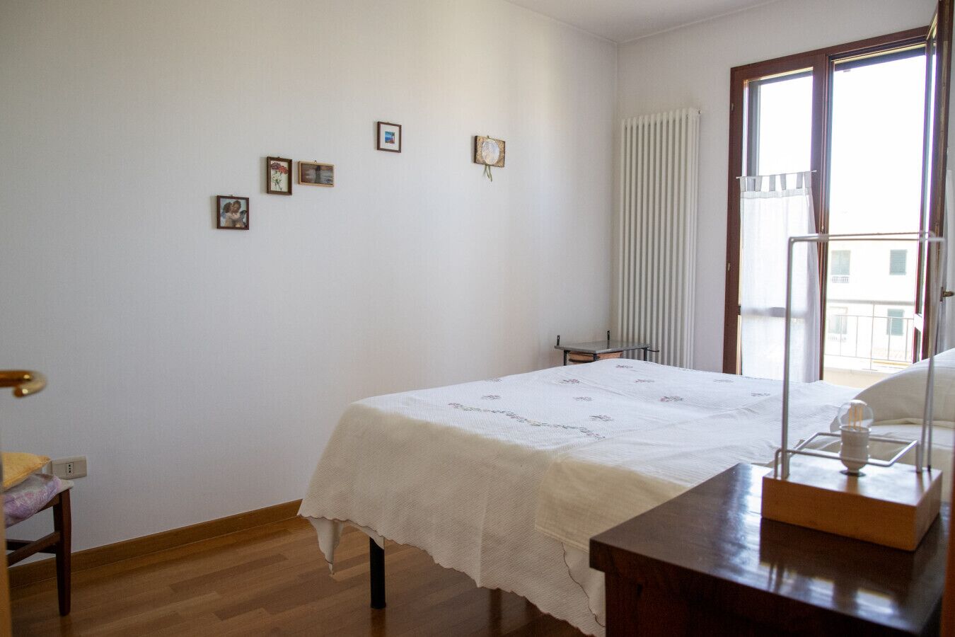 Ein Schlafzimmer mit Bett, Schreibtisch, Stuhl, Heizkörper und Fenster mit Blick.