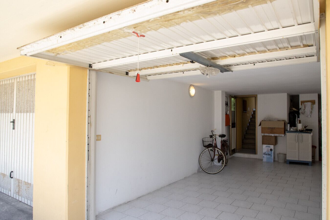 Een ruime garage met een fiets, een trap naar de tweede verdieping en een kitchenette.