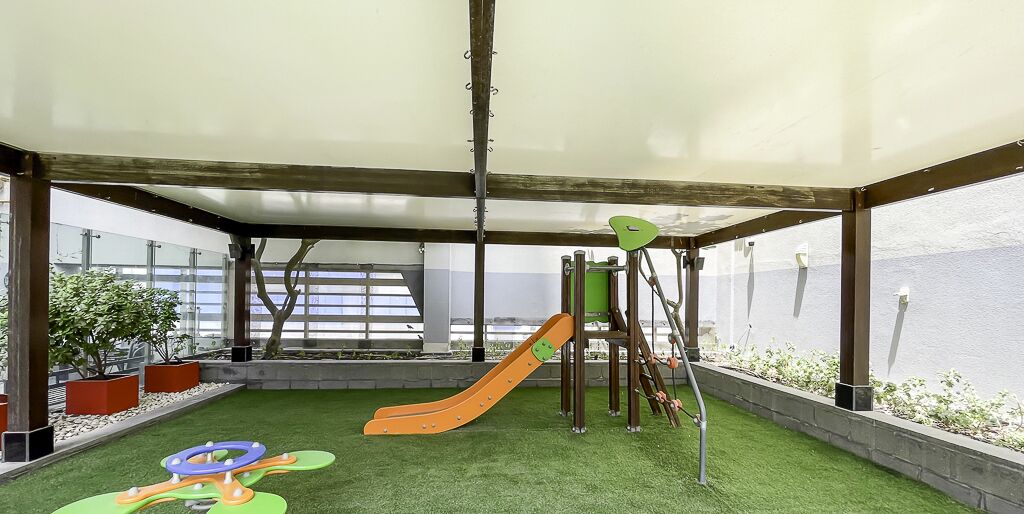 Un área de juegos al aire libre techada con un tobogán, estructuras para escalar y césped artificial.