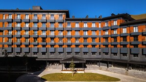 A modern multi-story building with a distinctive orange and grey facade, featuring balconies and a central courtyard with a small tree. - The NEO two room Suite N302 by MaRKoS (Gudauri)
