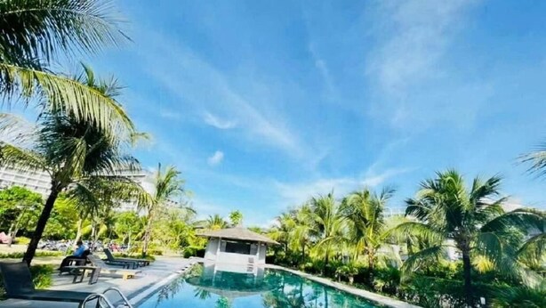 Une piscine à l’eau d’un bleu cristallin, entourée de palmiers et agrémentée d’un petit pavillon.