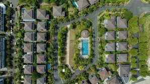 Vue aérienne d’un quartier résidentiel avec de nombreuses maisons, une piscine centrale et de la végétation luxuriante tout autour.