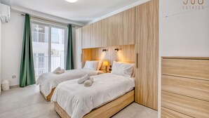 Ein modernes Hotelzimmer mit zwei Betten, einem Holzkopfende und einem großen Fenster mit Vorhängen.