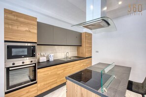 Una cuina moderna amb armaris de fusta, electrodomèstics d'acer inoxidable, una taula de dinar de vidre i un forn integrat.
