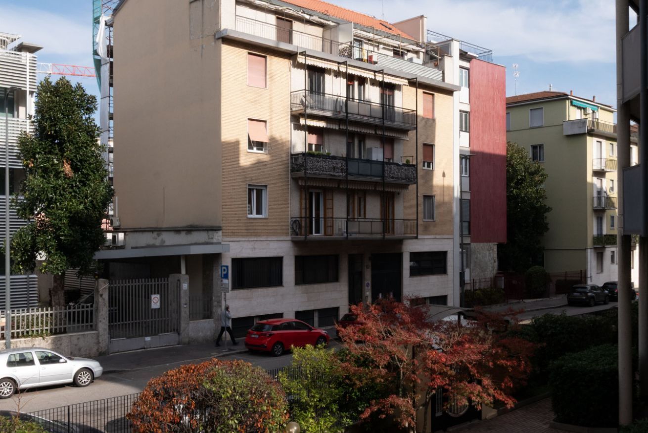 Un edificio residenziale a più piani con balconi, un'area parcheggio e un percorso pedonale.