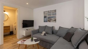 Ett modernt vardagsrum med en grå soffa, ett litet vitt bord och en platt-TV.