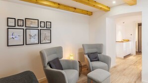 Una sala de estar moderna con dos sillones grises, una mesita de noche con una lámpara y obras de arte enmarcadas en la pared.