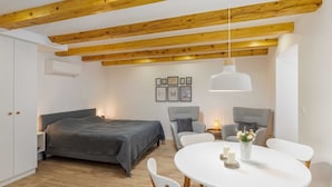 Un dormitorio moderno con cama, mesitas de noche, una mesa redonda de comedor con sillas y un techo con vigas de madera a la vista.