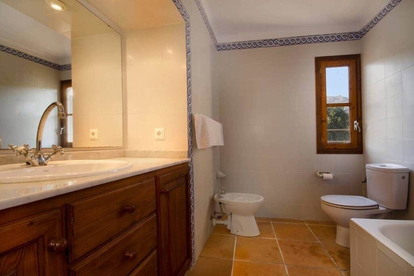 Een badkamer met een grote spiegel, twee wasbakken, een toilet en een bad.