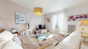 Ein modernes Wohnzimmer mit einem Flachbildfernseher, weißen Möbeln und Kunstwerken an den Wänden.