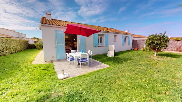 A house with a patio area featuring a table and chairs, a red umbrella, and a small garden.