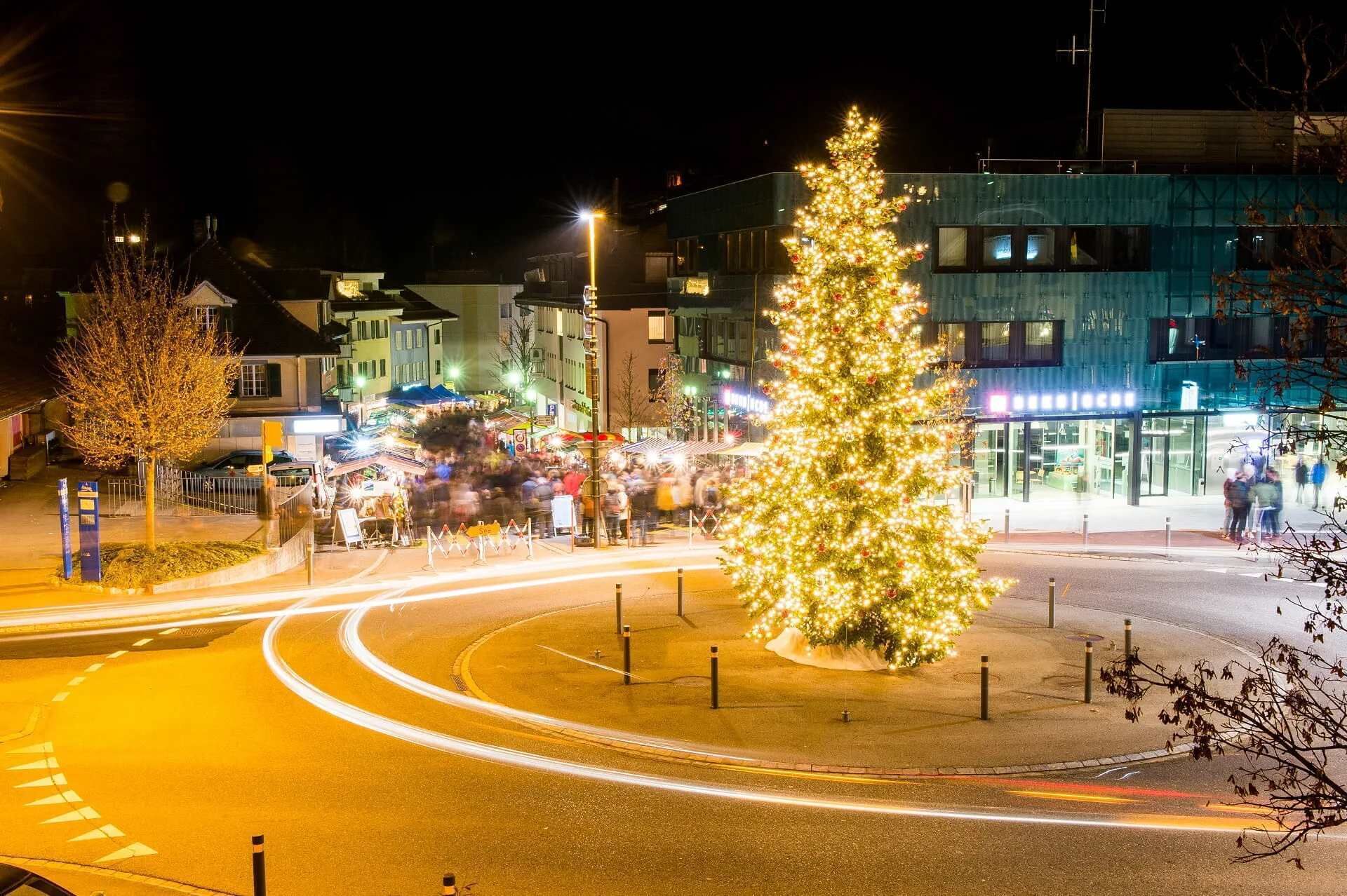 Un árbol de Navidad en una plaza pública con una glorieta y edificios al fondo.