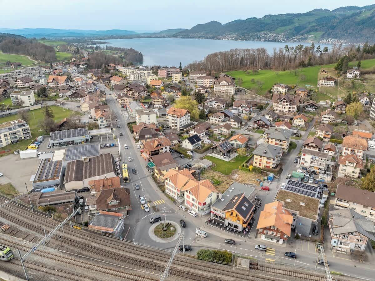 An aerial view of a town with residential buildings, a railway station, and a lake in the background.