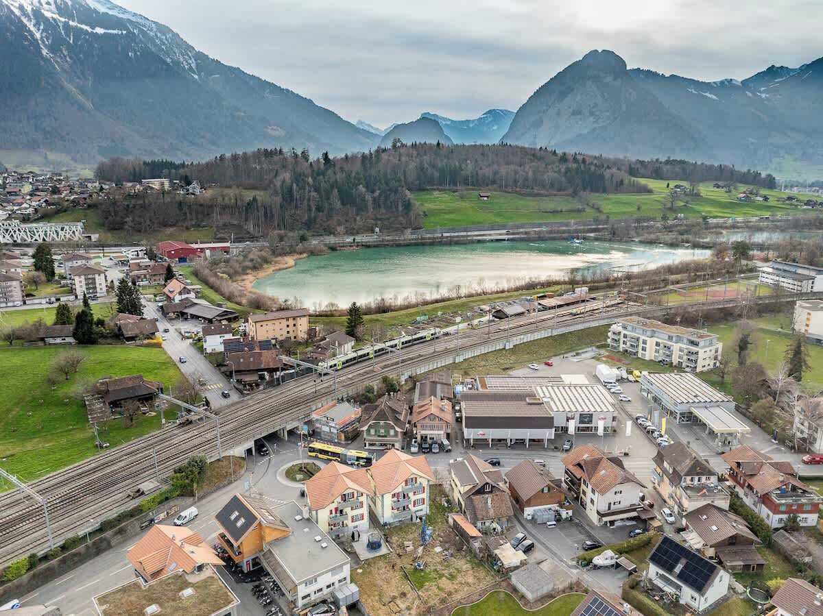 Vista aérea de un pueblo con una estación de tren, un río y montañas al fondo.