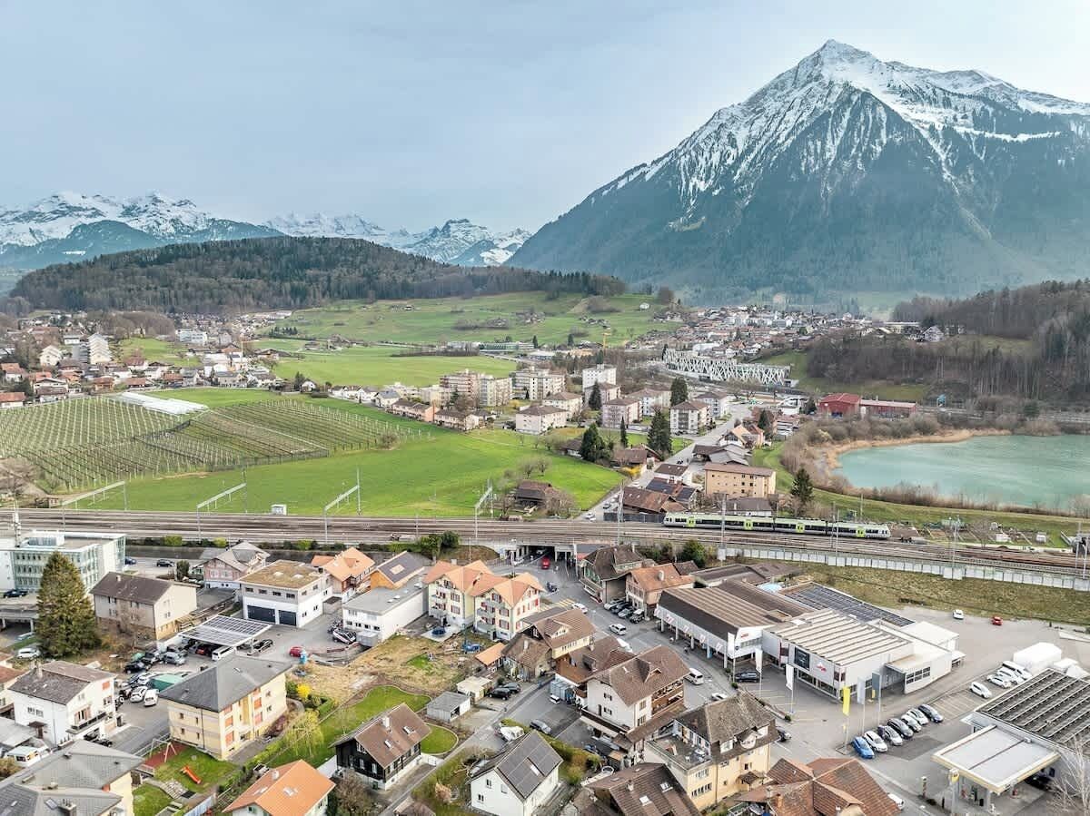 Une vue aérienne d’une ville avec des immeubles résidentiels, une gare et un paysage montagneux en arrière-plan.