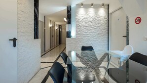 Una habitación de hotel moderna con una mesa de comedor de vidrio, sillas negras, una silla blanca, un pilar de mármol, una pared con textura y una puerta con un letrero de número.