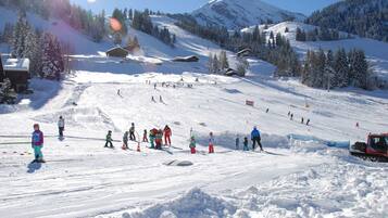 A snowy ski slope with skiers and a snow groomer.