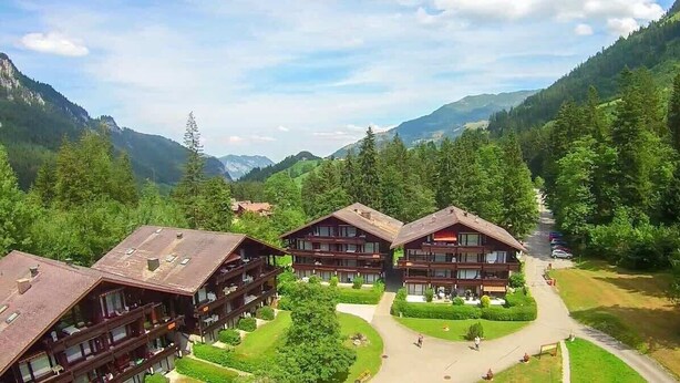 Un chalet composé de plusieurs bâtiments en bois, entouré d’une végétation luxuriante et de montagnes.