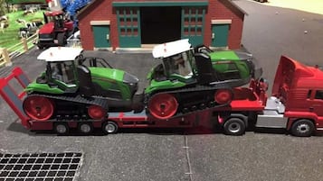Un'azienda agricola modello con due trattori verdi e un camion rosso parcheggiati davanti a un edificio con un cartello che riporta la scritta "siku".