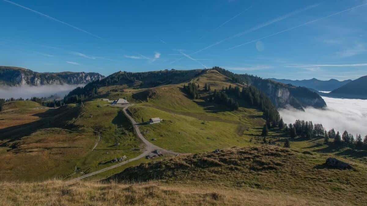 Un paisaje montañoso con cielo despejado, una carretera sinuosa y un edificio pequeño.