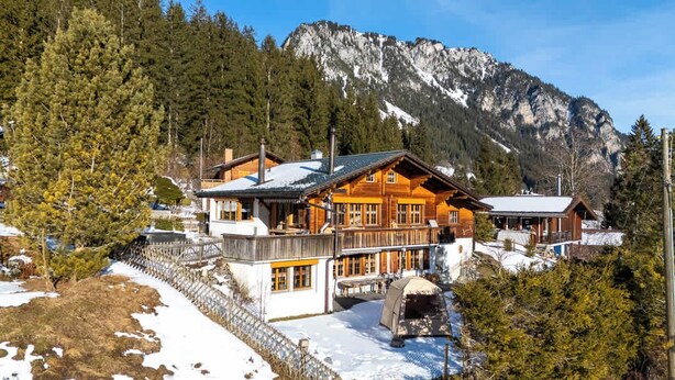 A log cabin with a balcony, surrounded by snow and trees, with a mountain in the background. - With Hot Tub, Sauna, Garden|with View near Gondola (Diemtigen)