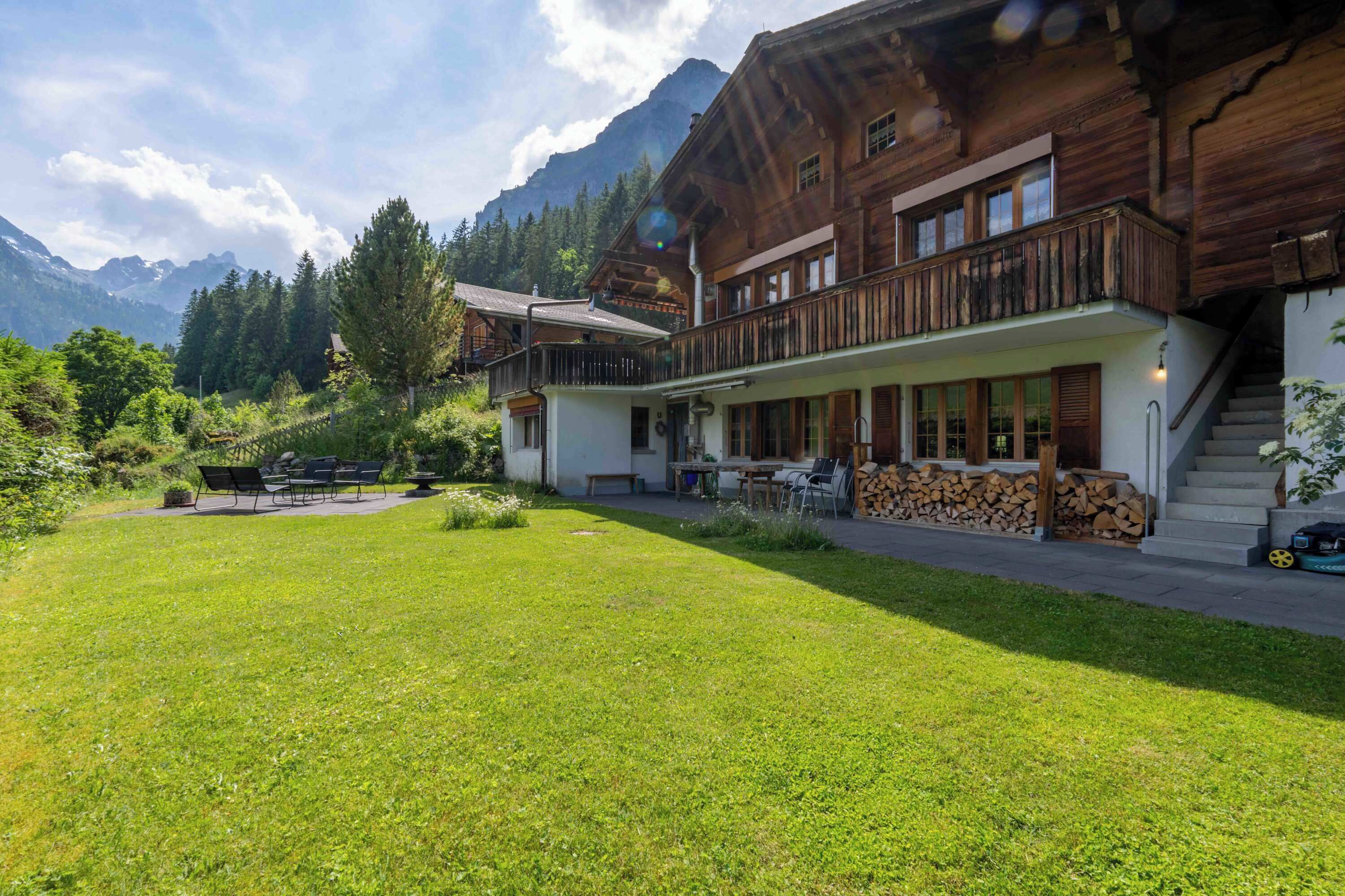 A wooden chalet with a balcony, a covered patio, and a mountain backdrop.