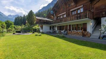 A wooden chalet with a balcony, a covered patio, and a mountain backdrop.