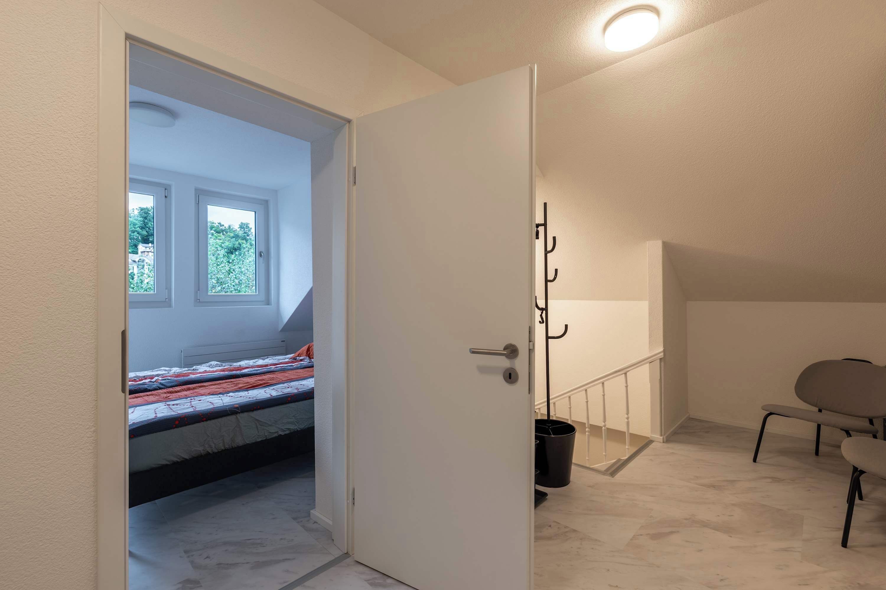 Un dormitorio con cama, una puerta que da a un balcón, una silla y un cesto de basura.